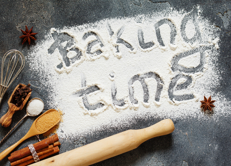 The process of baking. Flour sprinkled on the gray table with text baking time. Baking ingredients flour, sugar, salt, eggs and spices on grey background, top viewの写真素材
