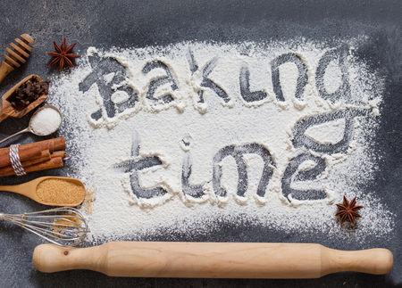 The process of baking. Flour sprinkled on the gray table with text baking time. Baking ingredients flour, sugar, salt, eggs and spices on grey background, top viewの写真素材