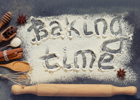 The process of baking. Flour sprinkled on the gray table with text baking time. Baking ingredients flour, sugar, salt, eggs and spices on grey background, top viewの写真素材