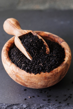 Black cumin or nigella sativa or kalonji seeds in bowl with spoon on black slate background, selective focusの写真素材