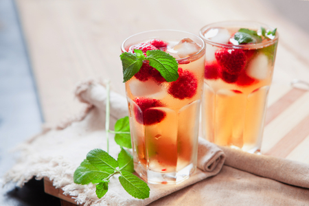 Refreshing summer drink with syrup, raspberry, mint and ice. Glasses with cold and healthy beverage, place for textの写真素材