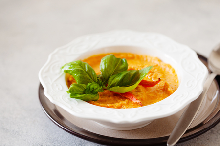 Curried carrot soup with cream and fresh basil on white tableの写真素材