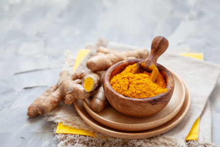 Turmeric powder in wooden bowl and fresh turmeric on light grey backgoundの写真素材