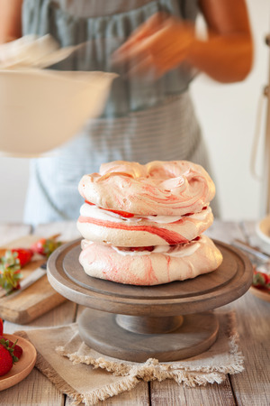 Woman decorating meringue cake with whipped cream and fresh strawberry. Cooking Pavlova cakeの写真素材
