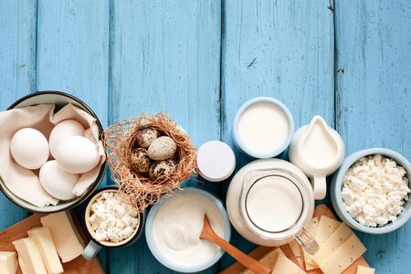 Different types of dairy products on blue wooden background: milk, sour cream, cottage cheese, cheese, cream, yogurt, eggs and butter. Top view with copy spaceの写真素材
