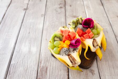 healthy fruit tropical salad served in half of yellow pitaya on wooden background, copy spaceの写真素材