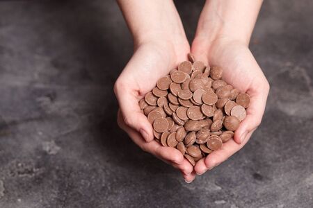 Milk chocolate chips in woman's hands top view
