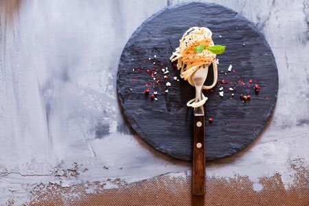Fork with classic italian spaghetti pasta with basil and cheese on dark slate board top view