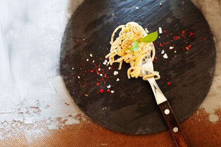 Fork with classic italian spaghetti pasta with basil and cheese on dark slate board top viewの写真素材