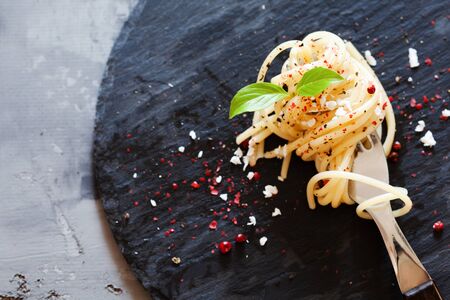 Fork with classic italian spaghetti pasta with basil and cheese on dark slate board top view with place for textの写真素材