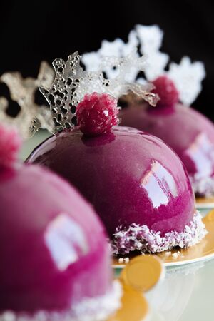 Close up of individual blueberry mousse cakes with mirror glaze, meringue and isomalt decoration