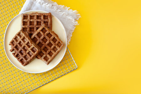 Homemade oat flour waffles served on a simple white plate, placed on a bright sunny yellow...