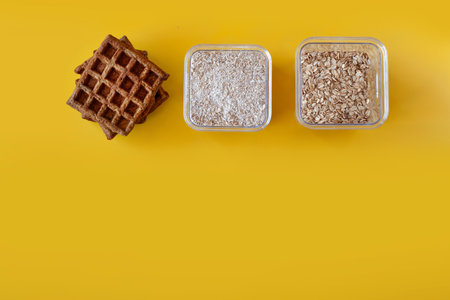 Oat flour waffles served on a simple white plate, placed on a bright sunny yellow background. Healthy breakfast concept, minimalistic food composition with warm natural lightの写真素材