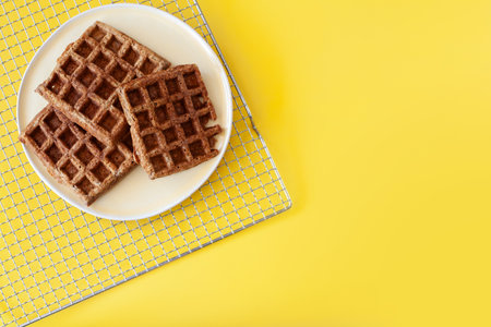 Homemade oat flour waffles served on a simple white plate, placed on a bright sunny yellow...