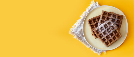 Homemade oat flour waffles served on a simple white plate, placed on a bright sunny yellow background. Healthy breakfast concept, minimalistic food composition with warm natural lightの写真素材