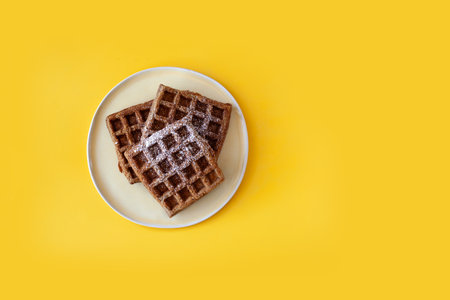 Homemade oat flour waffles served on a simple white plate, placed on a bright sunny yellow background. Healthy breakfast concept, minimalistic food composition with warm natural lightの写真素材