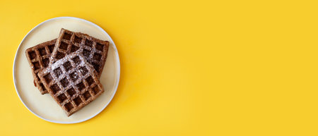 Homemade oat flour waffles served on a simple white plate, placed on a bright sunny yellow background. Healthy breakfast concept, minimalistic food composition with warm natural lightの写真素材