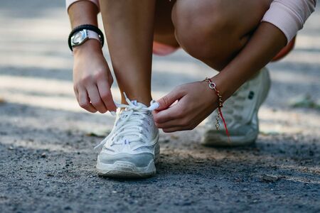 Female hands tying shoelaces of white sneakers on the street before the running training