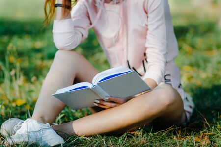 young woman with headphones in sports wear sitting on the grass in park reading a bookの写真素材