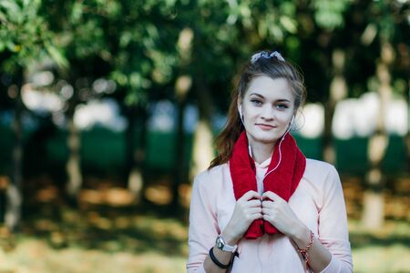 Young woman in sports wear standing with a towel on her shoulders and smiling after training in the...