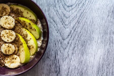 Plate of oatmeal with apple, banana, cinnamon and flax seeds stands on a gray wooden background. Top view. Copy space for text.の写真素材
