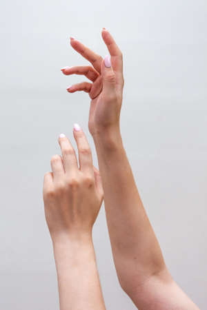Crop view of a young womans hands raising up close-up on a light monochrome background. Healthy hands and nails.の写真素材