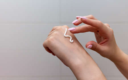 Close up of female hands applying moisturizing creme on the white tile background. Skincare and handcare concept. Cosmetic procedure.の写真素材