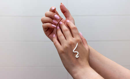 Close up of female hands with moisturizing creme on the white tile background. Skincare and handcare concept. Cosmetic procedure.の写真素材