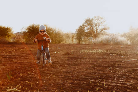 A boy rides a balance bike in a clearing. Spring mood. Sun