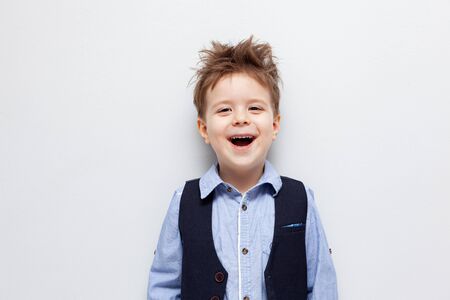 A boy with disheveled hair in a shirt, vest and trousers stands against a white background. The child is naughty.の写真素材