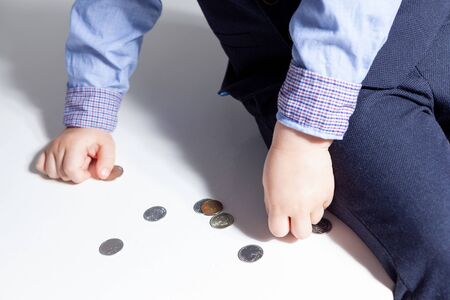 A boy in a shirt, bow tie, vest and trousers on a white background holds coins in his hands. Stylish baby with hair stylingの写真素材