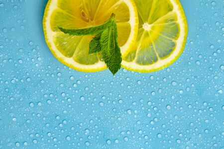 Composition with cut citrus fruits on blue background. Creative summer background composition with lemon slices, leaves mint and ice cubes. Minimal top down lemonade drink concept. Top viewの写真素材