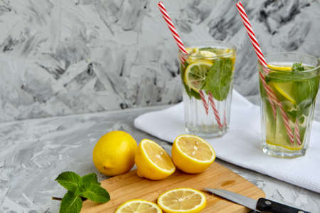The process of making lemonade. On a wooden Board is a Lemon and mint next to a knife. There are glasses of lemonade in the background. Summer drink. Lemonade with lemon and mint. Selective focusの写真素材
