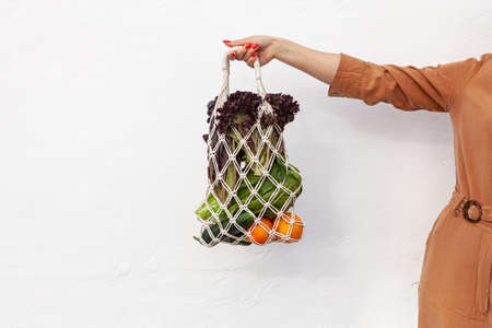 Girl is holding mesh shopping bag with vegetables, greens without plastic bags. Zero waste, plastic free Eco friendly concept. Handmade macrame bag. Sustainable lifestyle.の写真素材