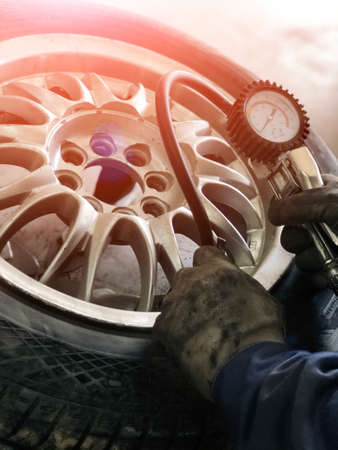 Auto mechanic man with electric screwdriver changing tire outside. Car service. Tire installation concept. Service maintenance car holding tire or tire car inspection for Measure quantity Inflated Rubber tires car.の写真素材
