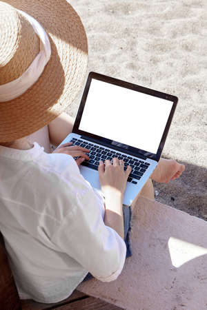Young woman using laptop computer on a beach. Freelance work concept. Pretty young woman using laptop in cafe on tropical beach in outdoor cafe terrace with sea view. Work and travelの写真素材