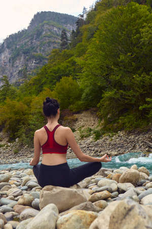 Yoga classes in nature. The concept of playing sports alone. Social exclusion. A woman does yoga on rocks, near a mountain river flowsの写真素材