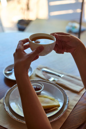 Cropped shot of person drinking tea and eating pancakes at wooden tableの写真素材