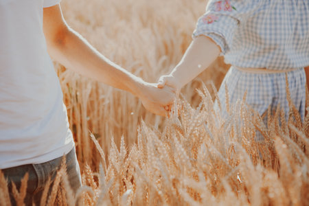 Couple taking hands and walking together in the nature. Concept love, date, emotion. A young couple, men woman, wheat fieldの写真素材