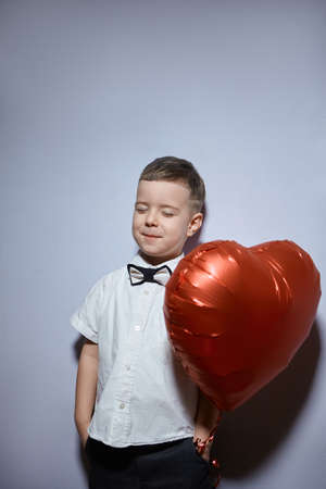 Valentine's day. Happy boy stands and holds red ball hearts on a white background.