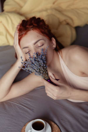 Very pretty redhead girl with dreads on bed in bedroom in the morning. A feminine, gentle girl. Coffee morning concept.の写真素材