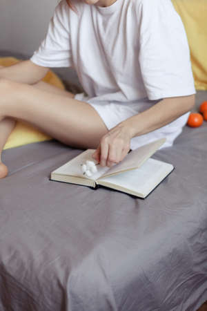 Very pretty redhead girl with dreads on bed in bedroom in the morning. Young woman reading a book sitting in bed. A feminine, gentle girl.の写真素材