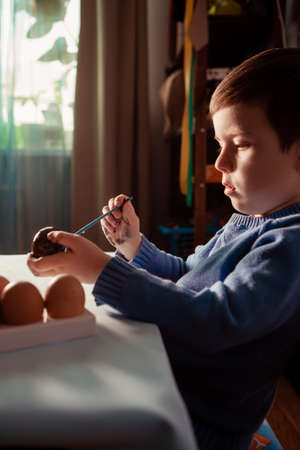Little Boy painting Easter Eggs with Paint at Home. Children's Easter creativity. A child decorate...