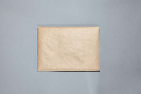 A brown craft envelope on gray background. Closed craft envelope, branch on gray table. Invitation card mockup. Flat lay, top view, copy space, mockupの写真素材