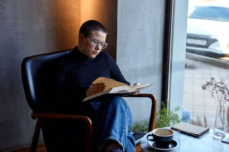 A young girl is sitting in a cafe reading a book. The concept of education and remote workの写真素材
