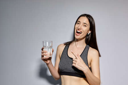 A woman in sports clothes and with wireless headphones drinks water. the concept of a healthy...