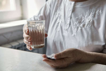 An elderly woman's hands unpacking several pills for taking medication. Grandma takes tablet and drinks a glass of waterの写真素材