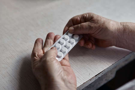 An elderly woman's hands unpacking several pills for taking medication.