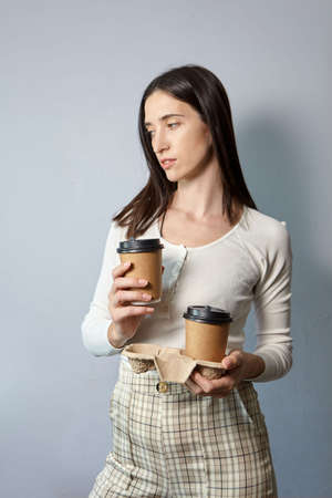 A woman in a white sweatshirt holds two cups of coffee. Tea or coffee to take away. Brown paper cup with black lid.の写真素材