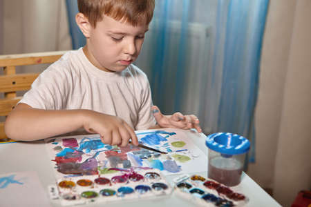 A boy draws with paints at a table in his roomの写真素材